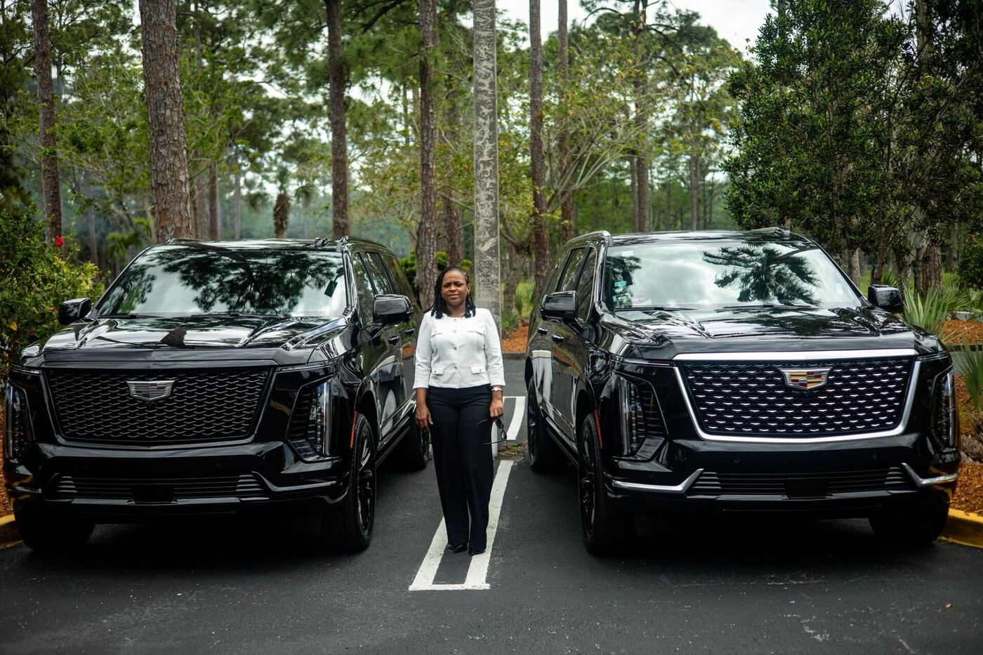 Female chauffeur standing between two black Cadillac Escalade ESVs