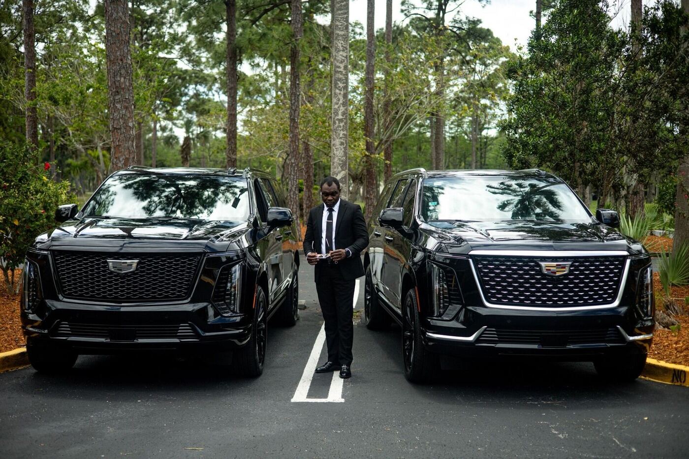 Owner standing between two black Cadillac Escalade ESVs