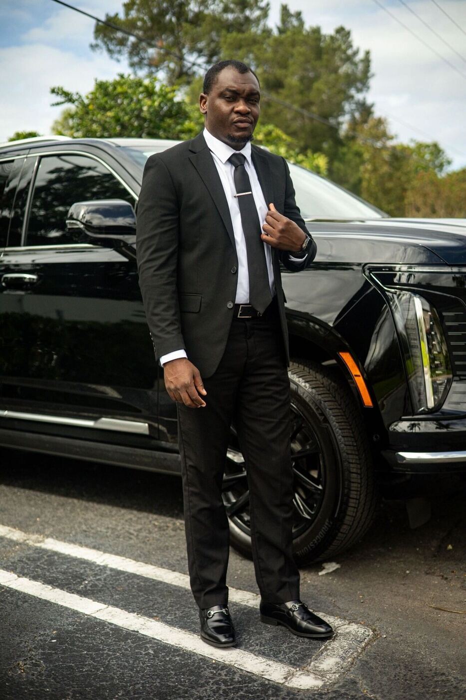 MS Luxury Black Car owner in a suit beside a black Cadillac Escalade